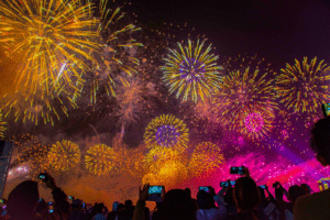 Fireworks in the night sky while people watch from the ground, holding their phones up.