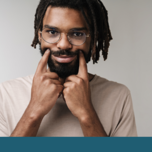 A person wearing glasses gently presses the corners of their mouth into a smile with both index fingers. The image illustrates the idea of masking, or changing outward expressions to appear a certain way despite how someone may actually feel. A teal banner runs along the bottom of the image.