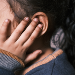 Close-up of a person covering one ear with their hand, suggesting sensitivity to sound or sensory overload.